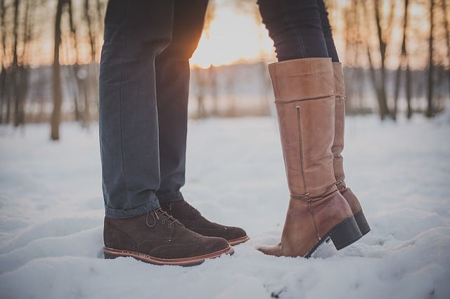 couples feet together standing in the snow, you can tell they are kissing but can only see up to their knees